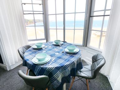 A dining table set for four with blue checkered tablecloth and turquoise dishes by windows overlooking a beach and sea at Apartment 3 in Tenby
