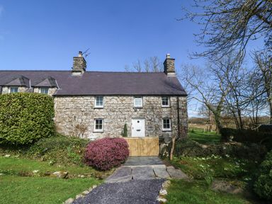 A stone cottage with a wooden gate and bushes in front at Y Bwthyn Ty Du in Pwllheli