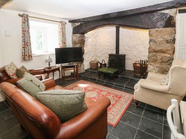 A living room with leather sofas a television and a fireplace with a wood burner at Y Bwthyn Ty Du in Pwllheli
