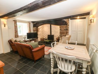 A living room with leather sofas a wood stove a dining table and chairs at Y Bwthyn Ty Du in Pwllheli