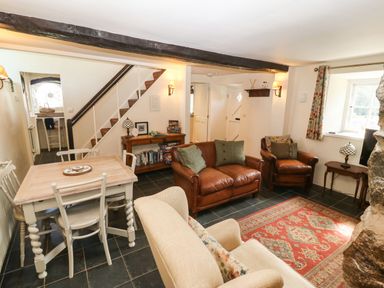 A living room and dining area with leather sofas a wooden dining table and an area rug at Y Bwthyn Ty Du in Pwllheli