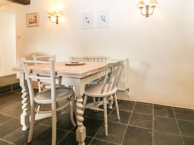 A dining area with a wooden table and four chairs on a tiled floor at Y Bwthyn Ty Du in Pwllheli