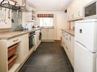 A kitchen with white cabinets a washing machine an oven a refrigerator and hanging utensils at Y Bwthyn Ty Du in Pwllheli