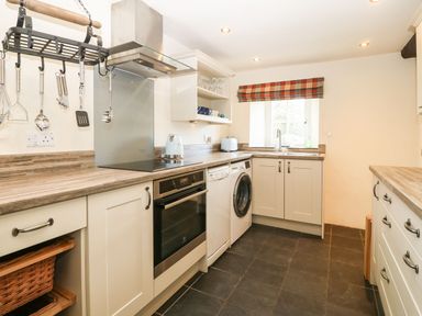 A kitchen with white cabinets appliances and a window with a plaid curtain at Y Bwthyn Ty Du in Pwllheli