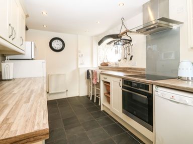 A kitchen with a stove microwave dishwasher hanging utensils and two chairs at Y Bwthyn Ty Du in Pwllheli