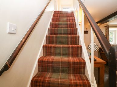 A staircase with plaid carpet and wooden handrails next to a room with a table and lamp at Y Bwthyn Ty Du in Pwllheli