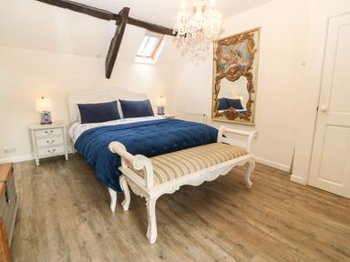 A bedroom with a large bed blue bedding two bedside tables lamps a bench an ornate mirror and wooden floor at Y Bwthyn Ty Du in Pwllheli