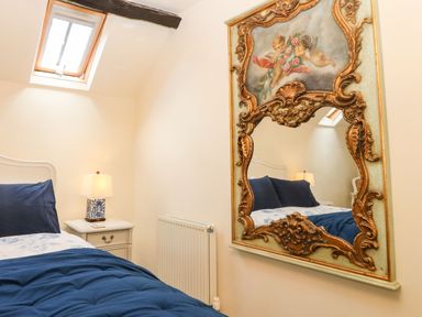 A bedroom with a blue bedspread a white nightstand with a lamp a skylight window and an ornate mirror on the wall at Y Bwthyn Ty Du in Pwllheli