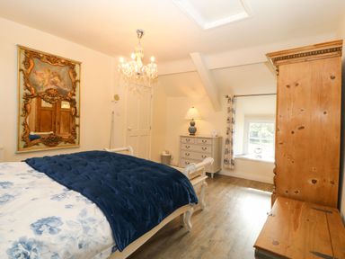 A bedroom with a bed a blue blanket a wooden chest and wardrobe and a chest of drawers with a lamp at Y Bwthyn Ty Du in Pwllheli