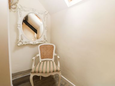 A chair with striped upholstery and a decorative mirror on the wall in a small room at Y Bwthyn Ty Du in Pwllheli