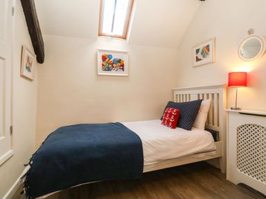 A small bedroom with a single bed a blue blanket colorful cushions a bedside table with a lamp and framed pictures on the walls at Y Bwthyn Ty Du in Pwllheli