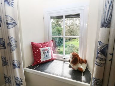A window seat with a red pillow featuring a dog and a stuffed dog toy at Y Bwthyn Ty Du in Pwllheli