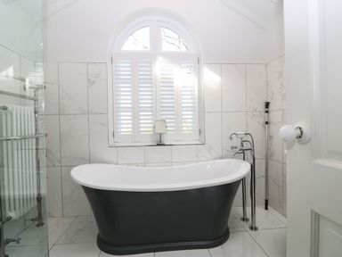 A bathroom with a black and white freestanding bathtub under a window with shutters at Y Bwthyn Ty Du in Pwllheli