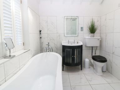 A bathroom with a bathtub a sink with a mirror a toilet and a plant on the toilet tank at Y Bwthyn Ty Du in Pwllheli