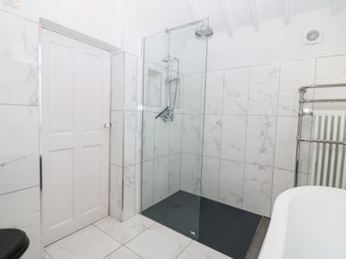 A bathroom with a walk-in shower with a glass partition and a black shower base at Y Bwthyn Ty Du in Pwllheli