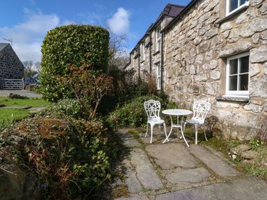 An outdoor patio with a white metal table and two chairs beside a stone building with a window at Y Bwthyn Ty Du in Pwllheli