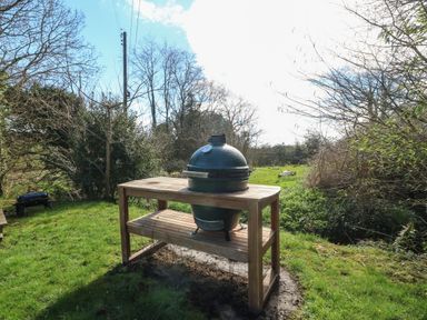 A green ceramic grill on a wooden table in a grassy outdoor area at Y Bwthyn Ty Du in Pwllheli
