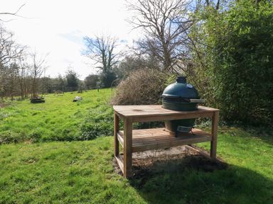 A green ceramic grill on a wooden table in a grassy backyard with trees and bushes at Y Bwthyn Ty Du in Pwllheli