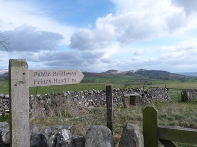 A wooden signpost for a public bridleway pointing to Friars Head with a stone wall and green fields with hills in the background at Woodpecker Lodge in Gargrave