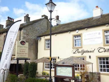 Exterior of Bollywood Cottage licensed Indian restaurant with signs and outdoor seating in a stone building