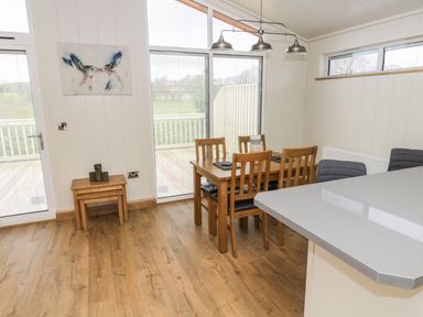 A dining area with wooden table and chairs next to sliding glass doors and a kitchen counter at Woodpecker Lodge in Gargrave