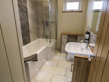 A bathroom with a bathtub shower combination and a sink with wooden cabinets at Woodpecker Lodge in Gargrave