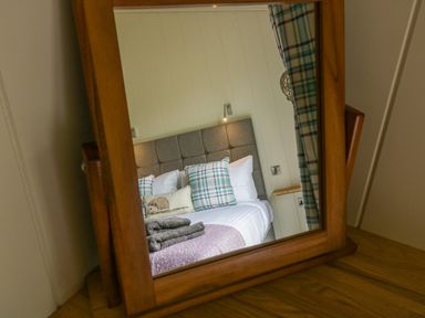A bedroom with a bed featuring plaid cushions and towels reflected in a wooden mirror at Woodpecker Lodge in Gargrave