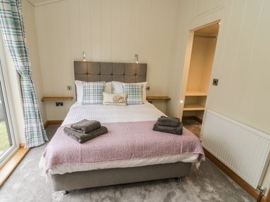 A bedroom with a bed with pillows and folded towels next to a window and an open closet at Woodpecker Lodge in Gargrave