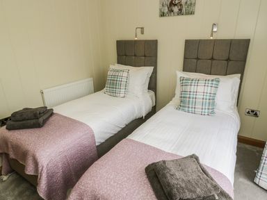 A bedroom with two single beds two plaid pillows and folded towels at Woodpecker Lodge in Gargrave