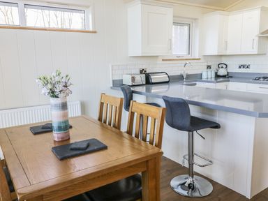 A kitchen and dining area with wooden table flowers on table and stools at Woodpecker Lodge in Gargrave