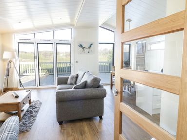 A living room with a grey sofa a wooden coffee table a floor lamp and large windows at Woodpecker Lodge in Gargrave
