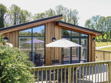 A wooden cabin with large windows and a patio table with an umbrella at Woodpecker Lodge in Gargrave