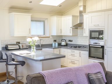A kitchen with white cabinets a countertop two bar stools and a vase with flowers at Woodpecker Lodge in Gargrave