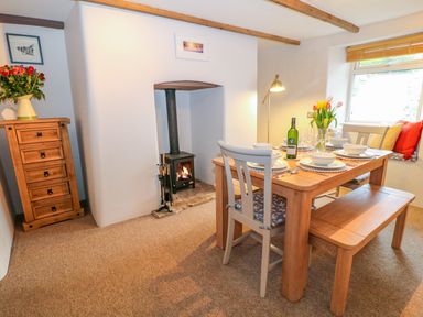 A dining room with a wooden table set for four near a window and a wood burning stove at Blue Anchor in Fraddon
