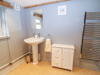 A bathroom with a pedestal sink a mirror a white cabinet a towel ring with a towel and a stainless steel heated towel rail at Blue Anchor in Fraddon
