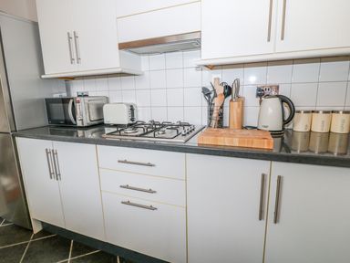 A kitchen countertop with a microwave a toaster a gas stove a utensil holder a knife block a kettle and canisters at Blue Anchor in Fraddon