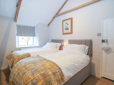 A bedroom with two single beds with gray headboards and patterned blankets by a window with a floral curtain at Blue Anchor in Fraddon