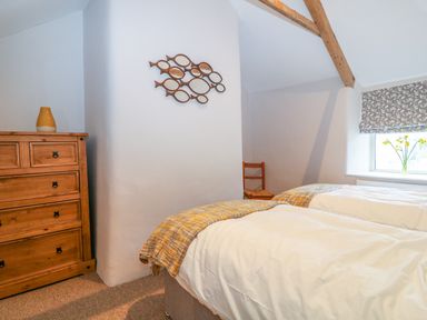A bedroom with two single beds a wooden chest of drawers a wooden chair and a window with flowers at Blue Anchor in Fraddon