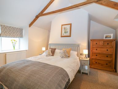 A bedroom with a bed bedside tables with lamps chest of drawers and a window at Blue Anchor in Fraddon