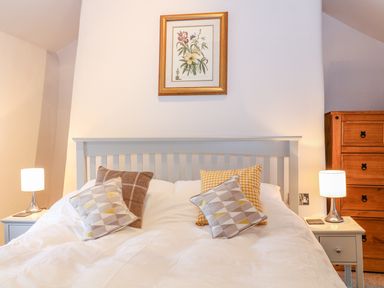 A bedroom with a bed with pillows two bedside tables with lamps a chest of drawers and a framed flower picture on the wall at Blue Anchor in Fraddon