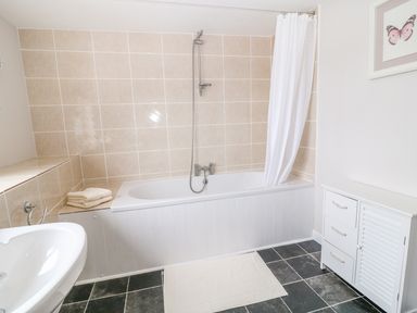 A bathroom with a bathtub shower sink cabinet white curtain and butterfly picture at Blue Anchor in Fraddon