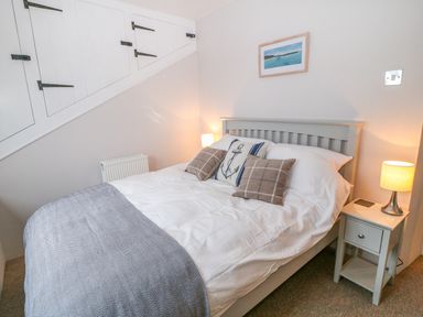 A bedroom with a double bed pillows bedside table lamps and under stairs storage at Blue Anchor in Fraddon