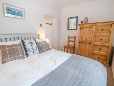 A bedroom with a bed with pillows a wooden chair a wooden cabinet and a mirror on the wall at Blue Anchor in Fraddon