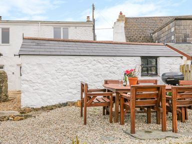 An outdoor patio with a wooden table and chairs a bottle of wine and flowers on the table outside a white stone house at Blue Anchor in Fraddon