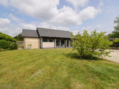 An exterior view of a single-story house with a lawn and a tree in front at The Barn at Daubeneys in Colerne