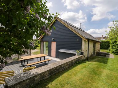 A house with dark siding and a pink door with a picnic table on a deck and grass surrounding the area at The Barn at Daubeneys in Colerne