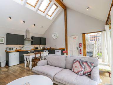 An open kitchen and living area with skylights a gray sofa wooden dining table and chairs at The Barn at Daubeneys in Colerne
