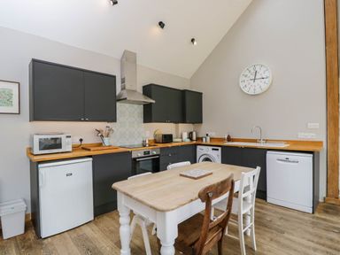 A kitchen with black cabinets wooden countertops a dining table with chairs and appliances at The Barn at Daubeneys in Colerne