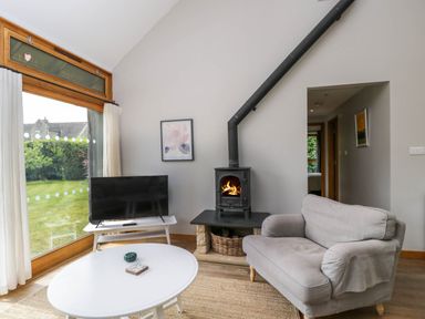 A living room with a gray armchair a white coffee table a black stove and a television near a large window at The Barn at Daubeneys in Colerne
