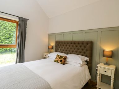 A bedroom with a bed with a tufted headboard two bedside tables with lamps and a window with curtains at The Barn at Daubeneys in Colerne